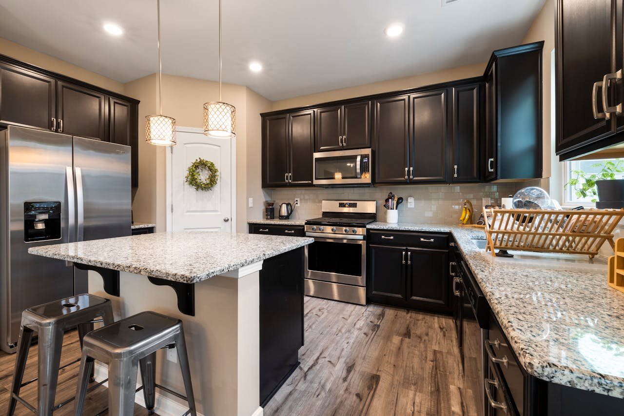 Stylish kitchen featuring black cabinets, granite countertops, and stainless steel appliances with elegant lighting.